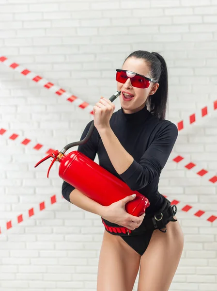 ボディスーツのセクシーな女性と赤い眼鏡のポーズレンガの白い壁に対して消火器で — ストック写真