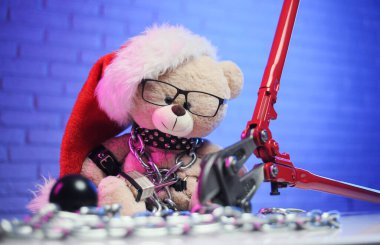 Noel 'de deri kemer takan bir oyuncak ayı ve Noel Baba şapkası zincirlenir ve BDSM oyunları için bir aksesuarı cıvata kesicinin yanına kelepçeler.