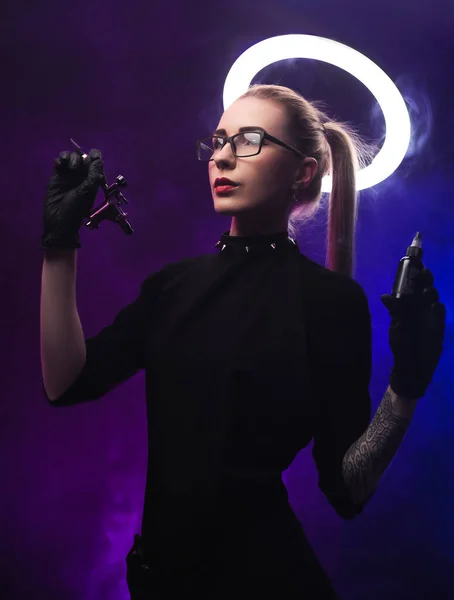 A woman with a halo in black clothes with a tattoo machine — Stock Photo, Image