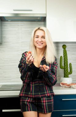 Mutfakta ev kıyafetleri içinde soyulmuş meyve püresi yiyen ve gülen bir kadın.