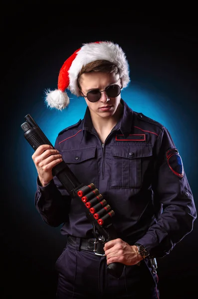 A man in a police uniform with a shotgun and a Santa hat for the new year holiday — Stock Photo, Image