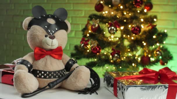 크리스마스 트리 배경에 있는 BDSM 을 위한 가죽끈 장치를 착용 한 장난감 곰 — 비디오