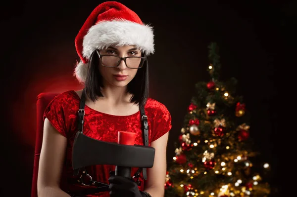 A woman in a red Christmas bodysuit and a Santa hat with an axe — Stock Photo, Image