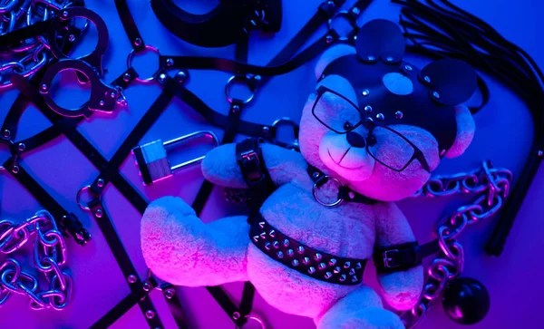 Urso de brinquedo vestido com cinto de couro arnês acessório para jogos BDSM em um fundo escuro em luz de néon — Fotografia de Stock