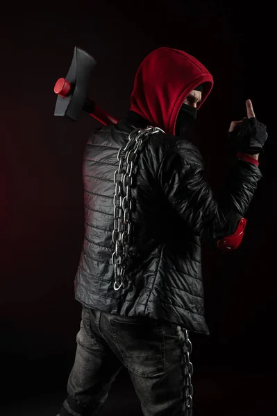 A man in a Balaclava and hoodies with an axe the image of a Protestant shows the middle finger — Stock Photo, Image
