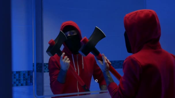 Um homem com o rosto coberto na sanita em frente a um espelho com um machado de incêndio está se preparando para um crime — Vídeo de Stock