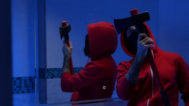 En man med ansiktet täckt i toaletten framför en spegel med en brandyxa förbereder sig för ett brott — Stockvideo