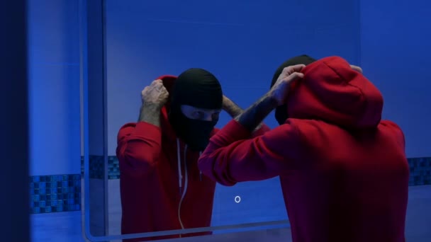 A man in the toilet in front of a mirror in a balaclava puts on a hood — Stock Video