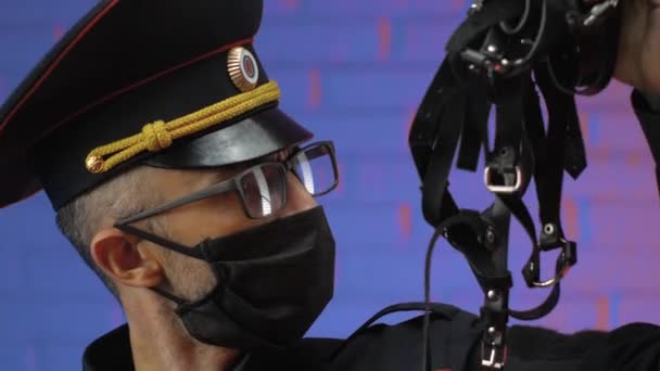 Een man in een militair politie-uniform met een coronavirusmasker kijkt verbaasd naar leren riemen en BDSM — Stockvideo