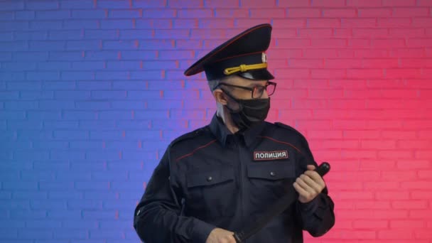 A man in a military uniform of the Russian police with a coronavirus mask cheerfully swings a baton and a weapon. English translation police, Russia — стоковое видео