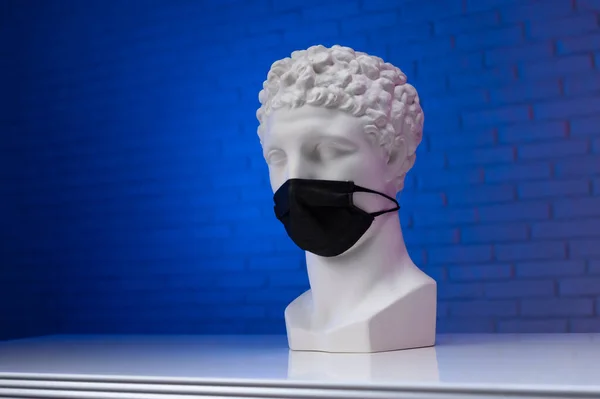 A white plaster statue wearing a disposable protective medical mask covering its face — Stock Photo, Image