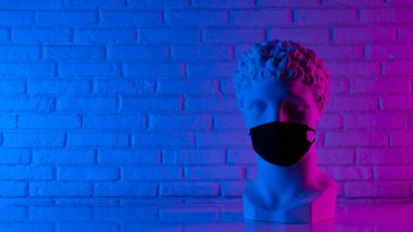 Tek kullanımlık koruyucu bir tıbbi maske takan beyaz bir alçı heykel yüzünü neon ışıkla kaplıyor.