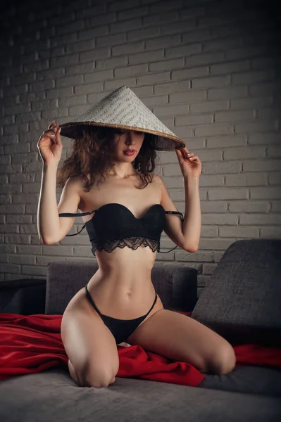 Стройная женщина в нижнем белье и азиатской шляпе на диване — стоковое фото