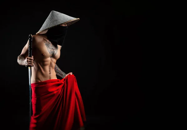 Un uomo nudo snello samurai in un mantello rosso e un cappello asiatico con una katana tatuata — Foto Stock