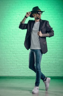 Ceketli, kovboy şapkalı şık bir adam stüdyoda poz veriyor.