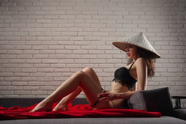 Slender sexy woman takes off her underwear and asian hat on the couch — Stock Photo, Image