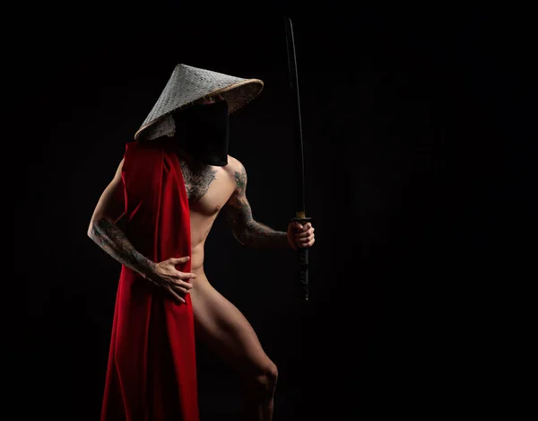 Nahý štíhlý muž samuraj v červené pláštěnce a asijský klobouk s tetovanou katanou — Stock fotografie