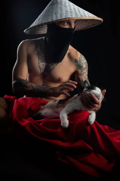 赤いマントを着た裸の細い侍と猫を手にしたアジアの帽子 — ストック写真