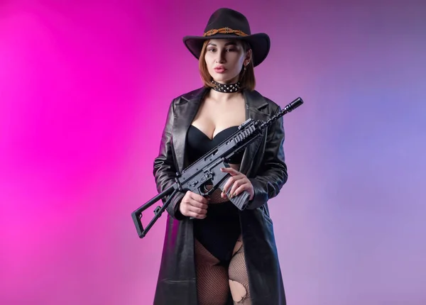 Stylová žena v černém oblečení a klobouk pózuje na neonovém pozadí s airsoftovou pistolí — Stock fotografie
