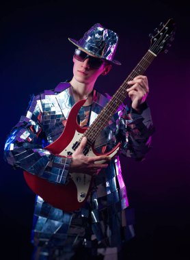 Aynalı takım elbiseli ve arka planda elektro gitarlı bir erkek sanatçı.