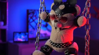 Oyuncak ayı zincirli bdsm aksesuarlarında neon ışıkta asılı.