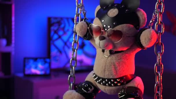 Oso de peluche suspendido de cadenas en accesorios bdsm en luz de neón — Vídeos de Stock