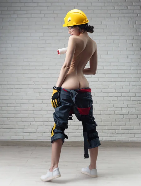 Una donna mezza nuda in tuta e un casco da costruzione con un rullo di vernice — Foto Stock