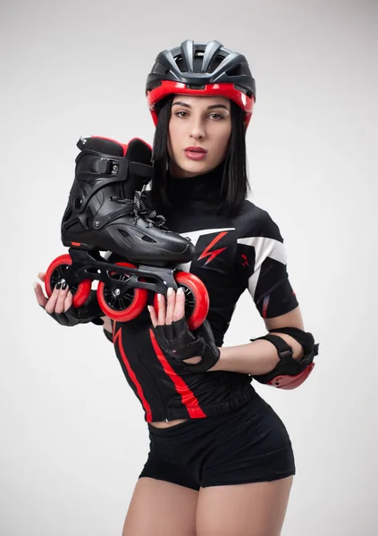 Femme mince en vêtements de sport et casque avec des patins à roulettes dans ses mains sur un fond blanc — Photo