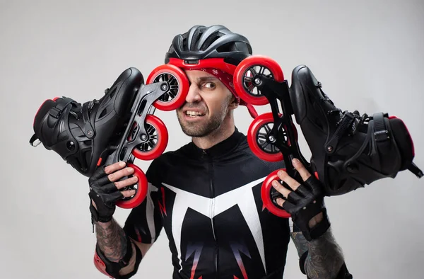 Un hombre con ropa deportiva y un casco con patines en las manos sobre un fondo blanco — Foto de Stock