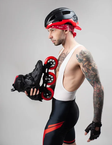 Un hombre con ropa deportiva y un casco con patines en las manos sobre un fondo blanco — Foto de Stock