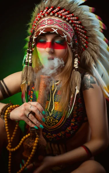 Uma mulher à imagem de um índio americano em uma capa de barata fuma um cachimbo — Fotografia de Stock