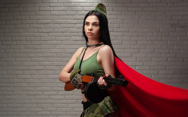 Una mujer en un sexy uniforme militar con un rifle de asalto PPSH-41 de la Segunda Guerra Mundial lleva una falda corta y cinturones de cuero y una bandera roja. — Foto de Stock