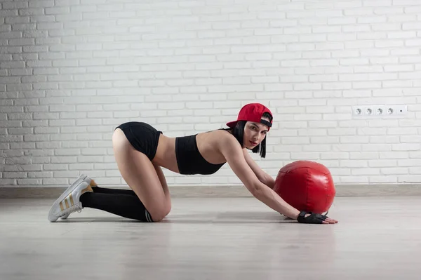 Athletic strong woman in sportswear trains with a fitness ball on a light background — Stock fotografie