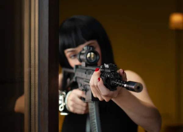 En kvinnlig lönnmördare på ett hotell nära fönstret siktar ett automatgevär med teleskopisk syn på offret som begår mord — Stockfoto