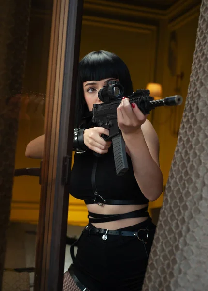 Женщина-киллер в отеле рядом с окном направляет автоматическую винтовку с телескопическим прицелом на жертву, совершившую убийство — стоковое фото