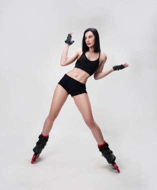 Beyaz arka planda dans eden, kısa spor elbiseli, paten giyen zayıf bir kadın.