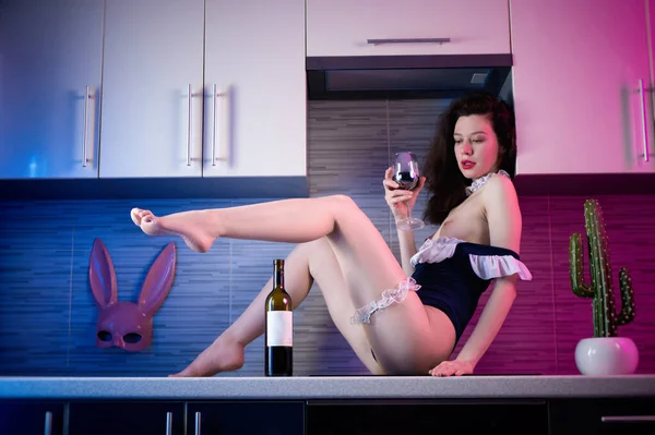 Стройная женщина в телесном костюме на кухне с бокалом вина на столе в неоновом свете сексуально возбуждает — стоковое фото