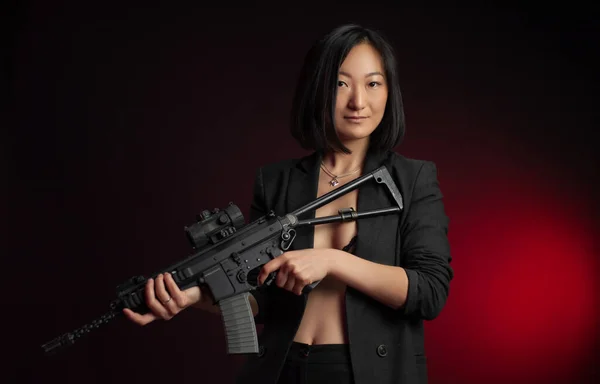 Mujer asiática en una chaqueta con un rifle automático en sus manos luchador mafia — Foto de Stock