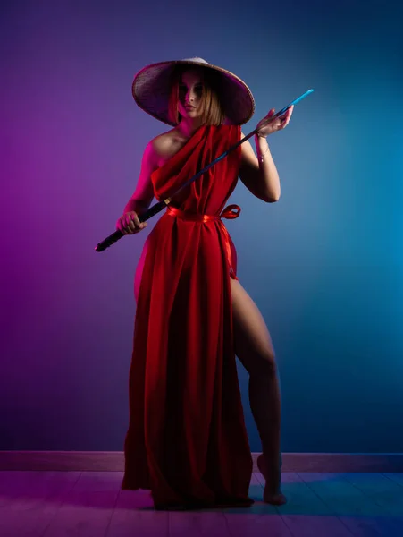Сексуальна жінка в червоному плащі і азіатський капелюх з катаною в руці зображення самурая в неоновому кольорі. — стокове фото