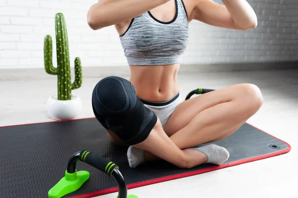 Una mujer deportiva en una rodillera fija para entrenamiento deportivo hace yoga en casa — Foto de Stock