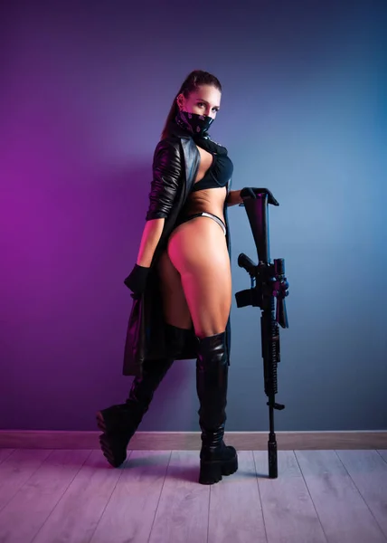 Sexy feminino assassino em roupa interior e uma capa de chuva de couro e sapatos de couro longo com um rifle automático m16 com uma visão telescópica — Fotografia de Stock