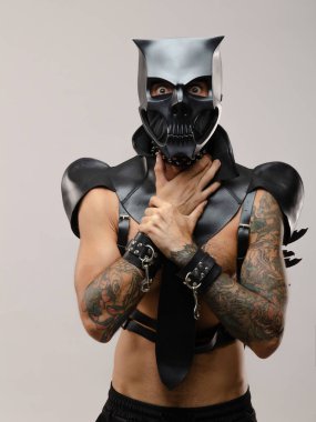 BDsm iblis kafatası maskeli bir adam deri bir pelerin giymiş ve vücudunda deri bilezikler ve kayışlar var.