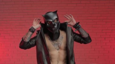 BDsm iblis kafatası maskeli bir adam deri bir pelerin giymiş ve vücudunda deri bilezikler ve kayışlar var.