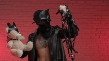 BDsm iblis kafatası maskeli bir adam deri bir pelerin giymiş ve vücudunda deri bilezikler ve kayışlar var.