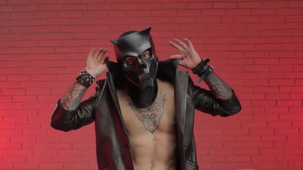 Ein Mann in einer bdsm Dämonen Totenkopfmaske, bekleidet mit einem Ledermantel mit Lederarmbändern und Riemen am Körper — Stockvideo