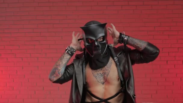 Ein Mann in einer bdsm Dämonen Totenkopfmaske, bekleidet mit einem Ledermantel mit Lederarmbändern und Riemen am Körper — Stockvideo