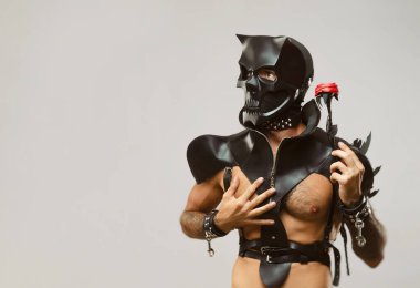 BDsm iblis kafatası maskeli bir adam deri bir pelerin giymiş ve vücudunda deri bilezikler ve kayışlar var.