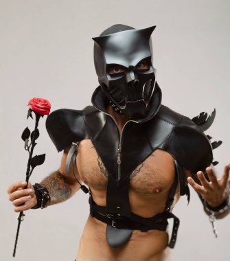 BDsm iblis kafatası maskeli bir adam deri bir pelerin giymiş ve vücudunda deri bilezikler ve kayışlar var.