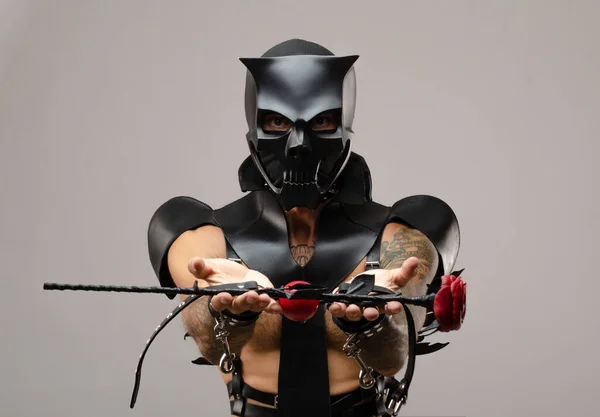 Egy férfi szado-mazo-ban koponya démon maszkot visel ostorral, bőresőkabátba öltözve bőrkarkötőkkel és szíjakkal a testén. — Stock Fotó
