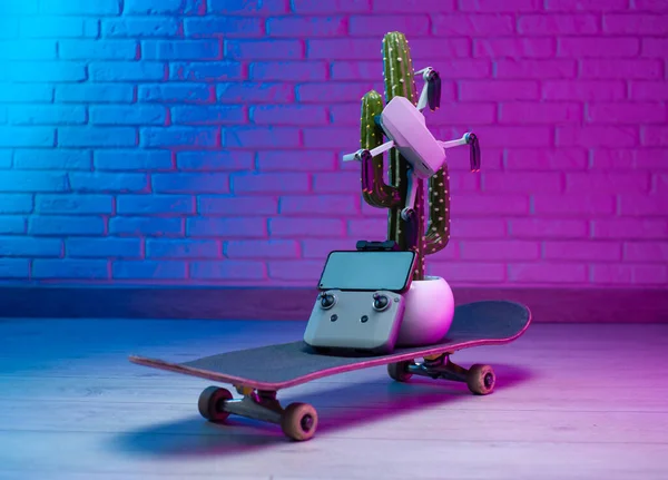 Un pequeño vehículo aéreo no tripulado se sienta en un cactus artificial, de pie en un monopatín en una idea creativa luz de neón —  Fotos de Stock